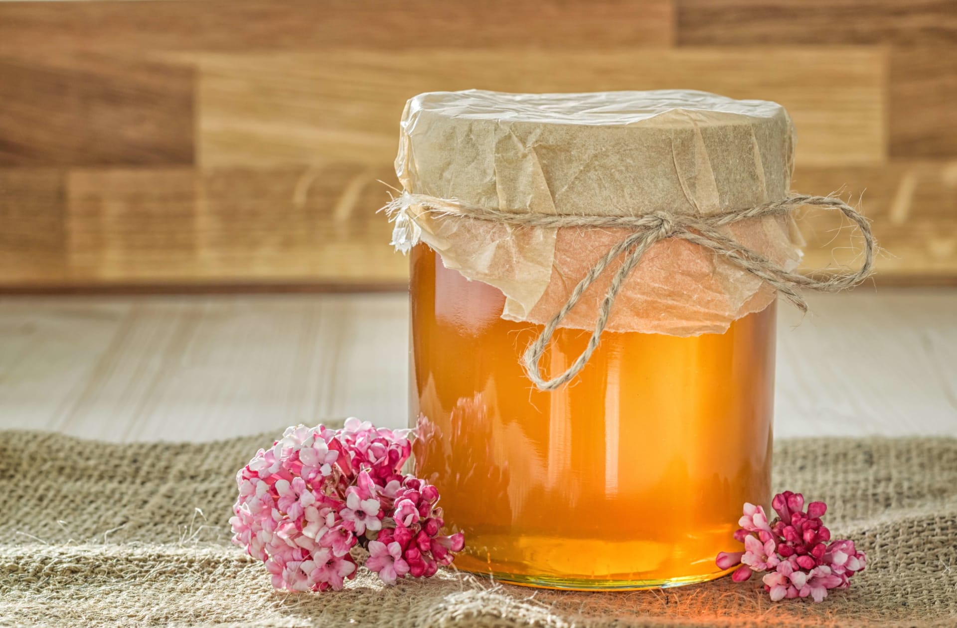 Farm table with pink flowers next to a jar of honey, Honig in German.
