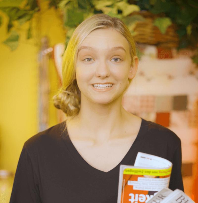 Woman smiling warmly and holding magazines in a German market.
