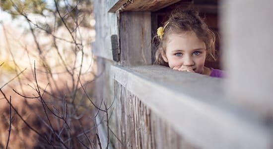 Young girl peaks out of a tree house.