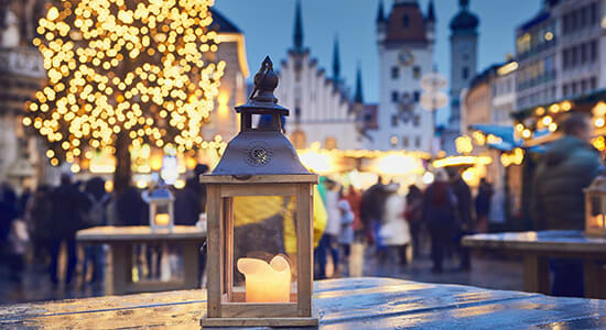 Traditional Christmas market in German city, with glowing lantern in front.